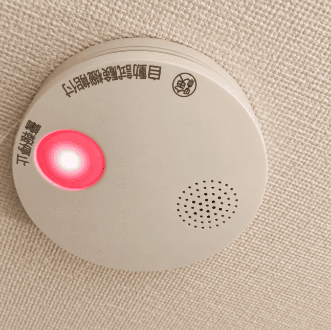 天井に取り付けられた家庭用火災報知器の赤いランプが点灯している様子
